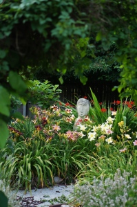 The Garden Lady is framed in day lilies and crocosmia.  The is the view from the entrance of the Secret Garden.