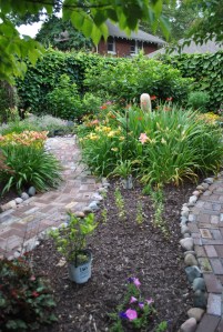 Rosie Returns day lily on the left, First Knight is the yellow lily across the path, crocosmia near the garden lady.